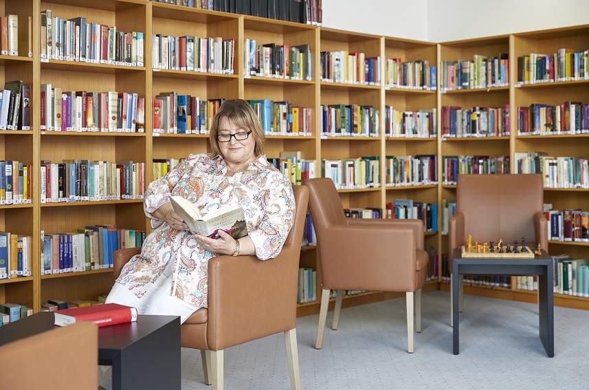 Eine Patientin der Knappschafts-Klinik Warmbad liest vor einem großen Bücherregal in einem Buch Eine Patientin der Knappschafts-Klinik Warmbad liest vor einem großen Bücherregal in einem Buch